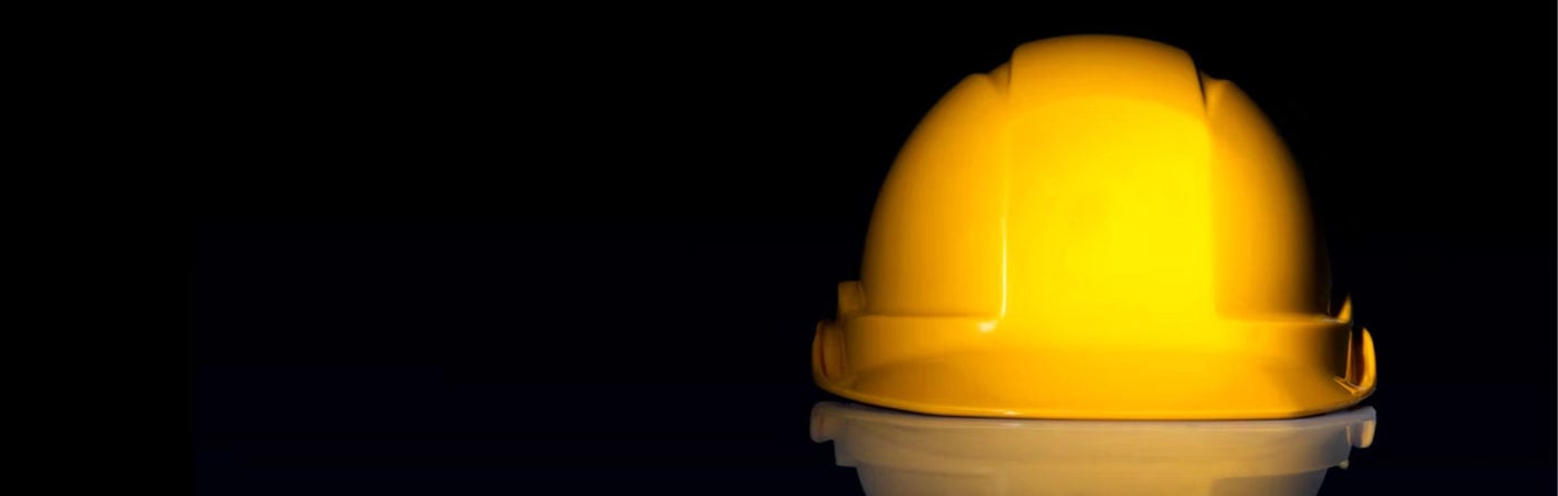 A yellow hard hat sits on a white base against a black background.