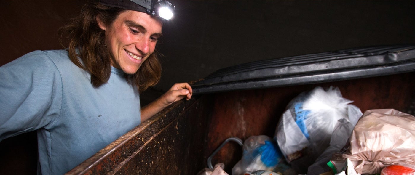 A man rummaging through a dumpster at night