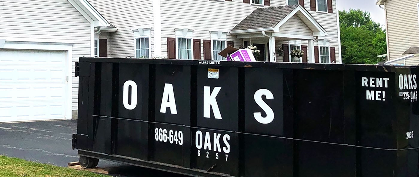 A large black dumpster with white text reading Oaks