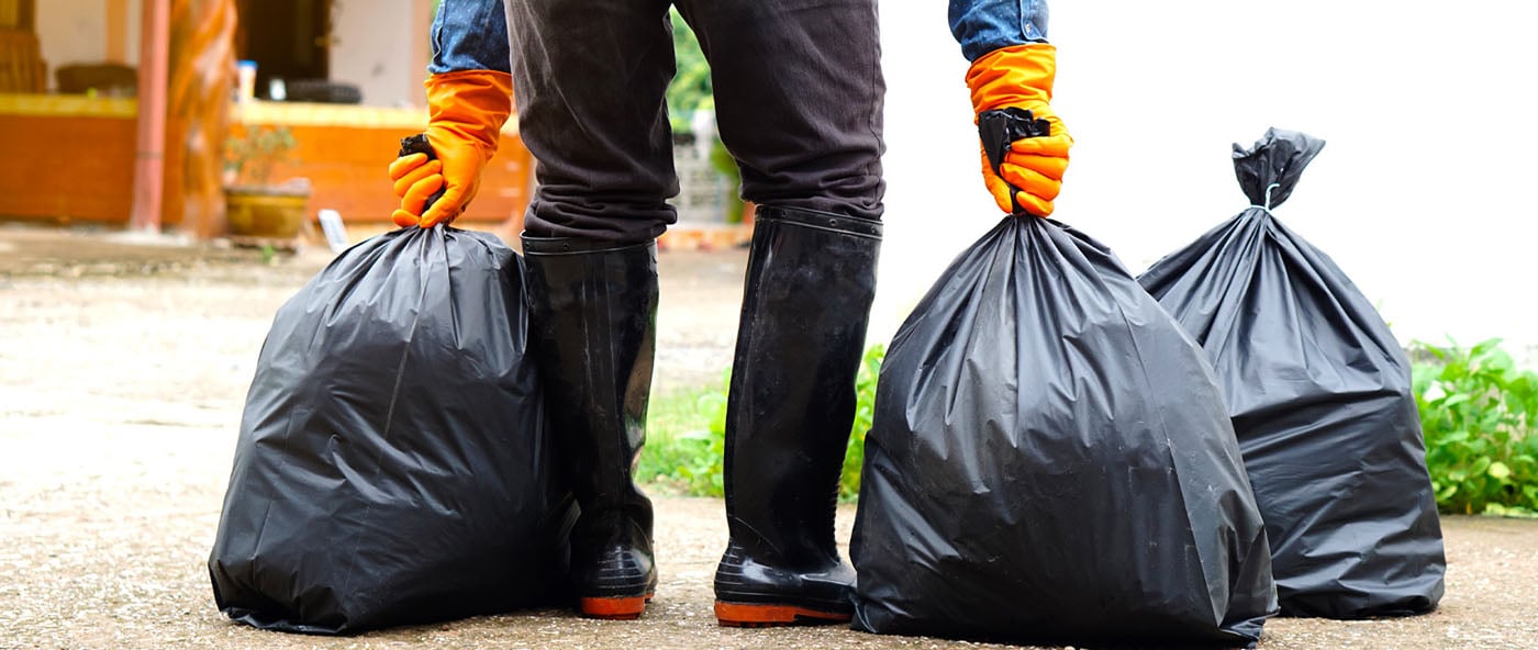 A person wearing gloves and boots holding trash bags.