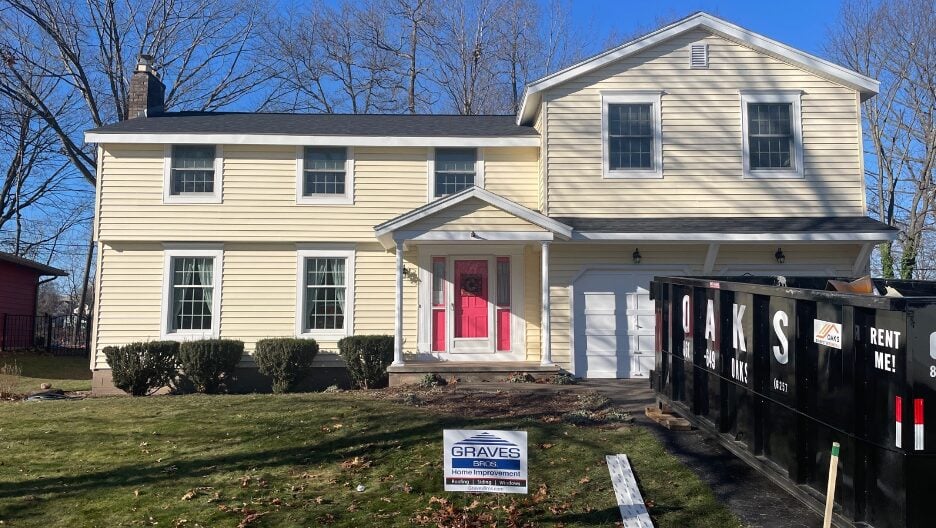A two-story house with a red door and a dumpster