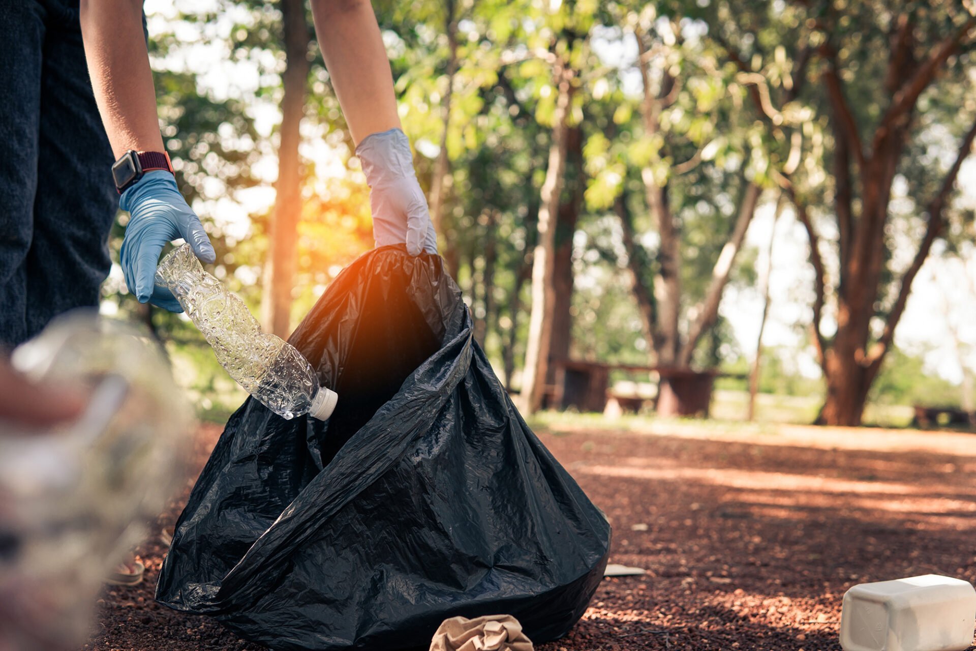 Person in gloves picking up a plastic bottle