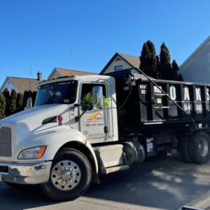 A white dump truck with a black bed parked on a street. The truck has a logo on the side.