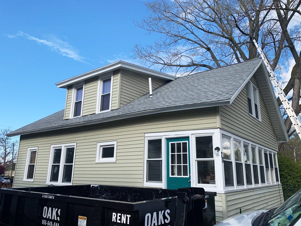 House with gray roof and green door house with construction dumpster
