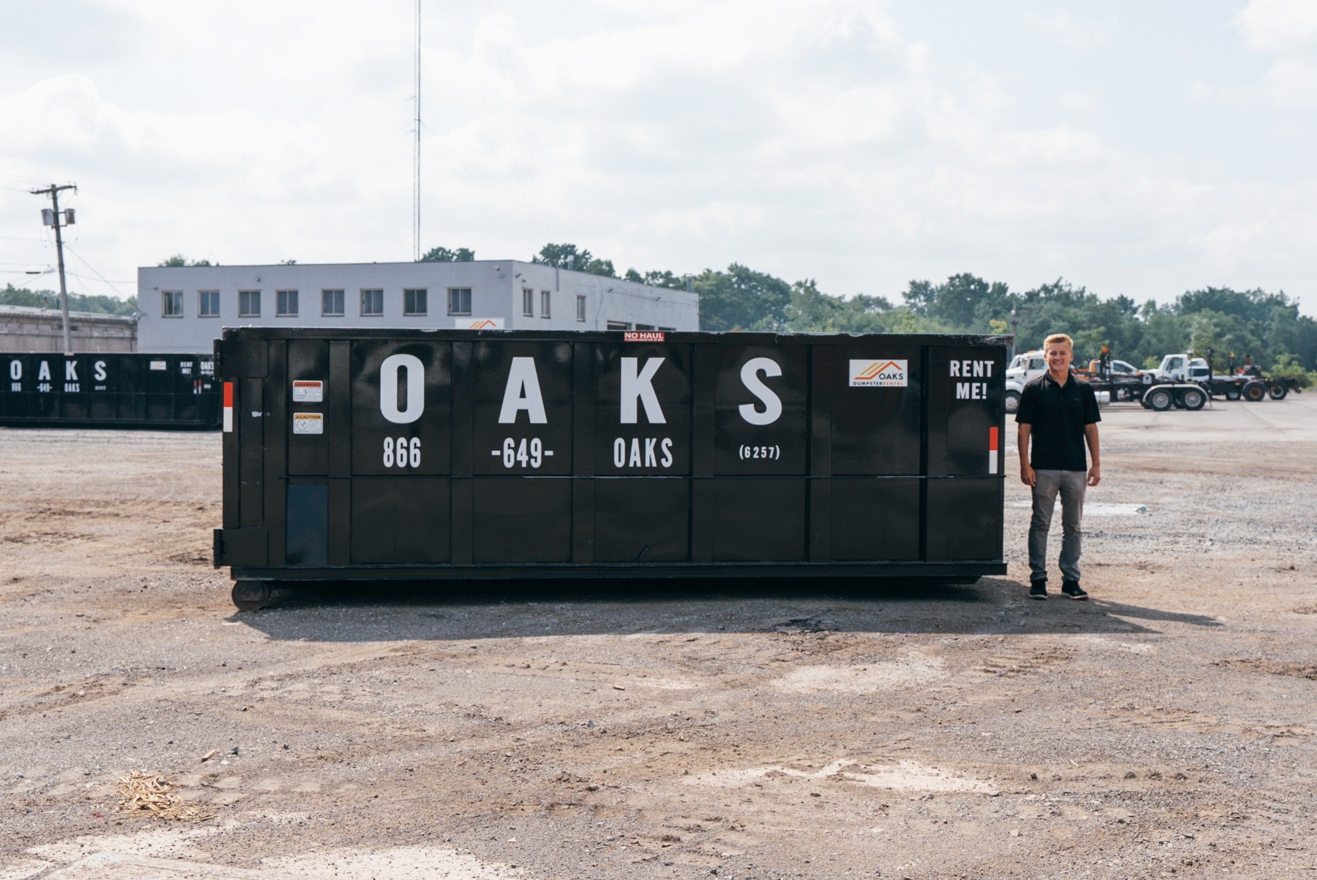 Man standing next to roll off-dumpster container. OAKS Construction.