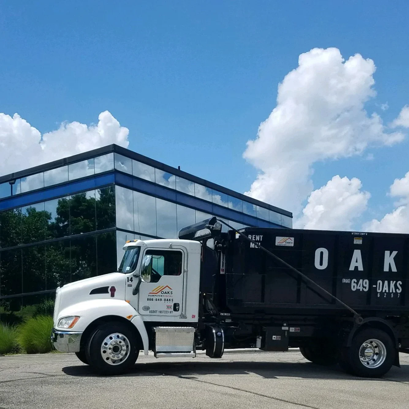 A white truck with a black dumpster parked outside.